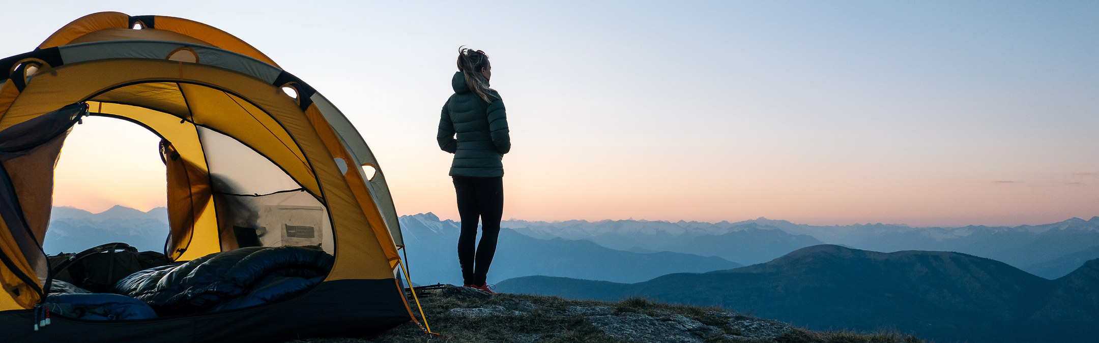 En kvinne står utenfor teltet og ser på utsikten utover fjellet.  
