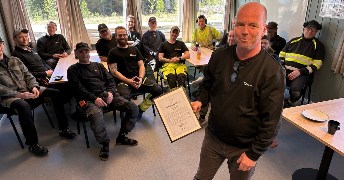 Kjell Rune Heia viser frem diplomet for Månedens bedrift i april. I bakgrunnen ansatte ved Containertech i Bygland – laget bakom anerkjennelsen.