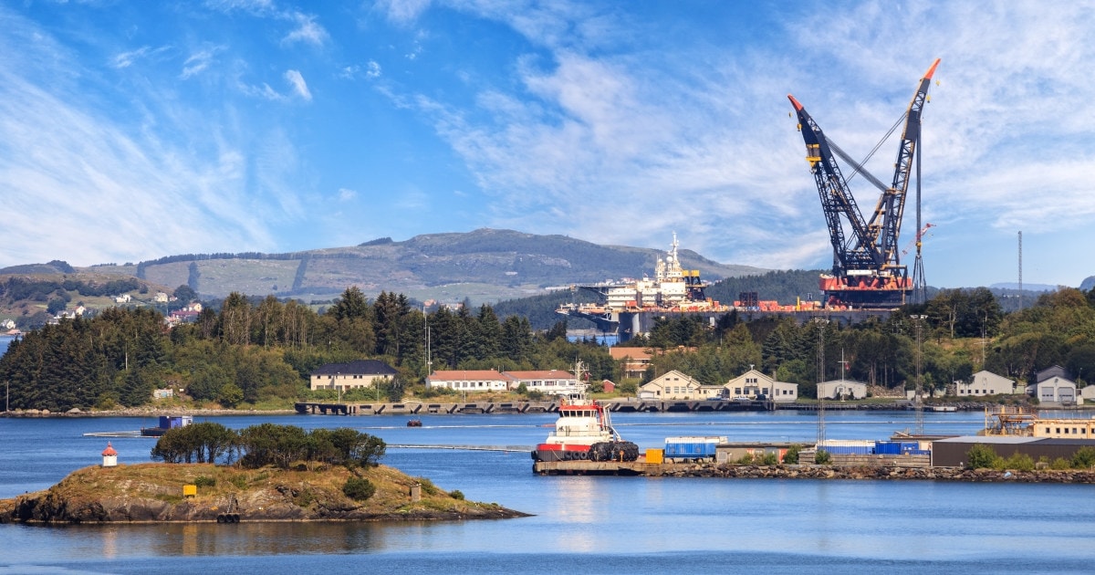 Havnebrygge med et svært kranskip i norsk kystlandskap.