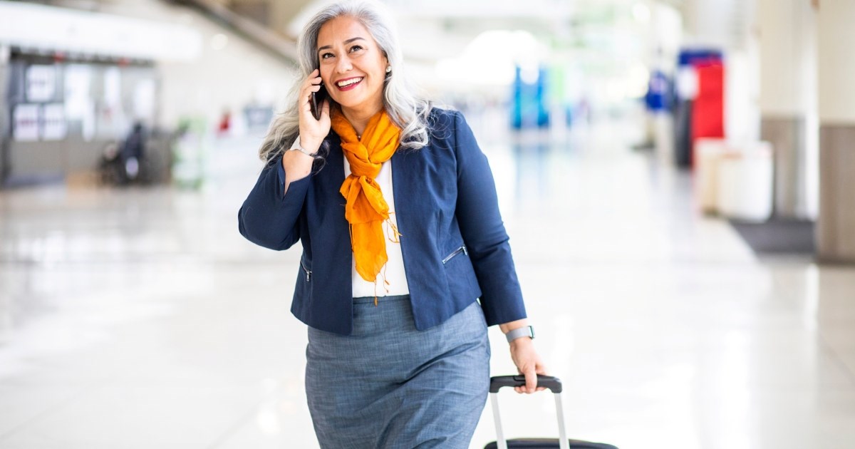 Eldre kvinner snakker i mobil mens hun går med en koffert.